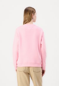 Rosa sweatshirt med rund hals, ribbede mansjetter og kant. Baksiden har en V-formet yoke detalj. Kombinert med lysebrune bukser.