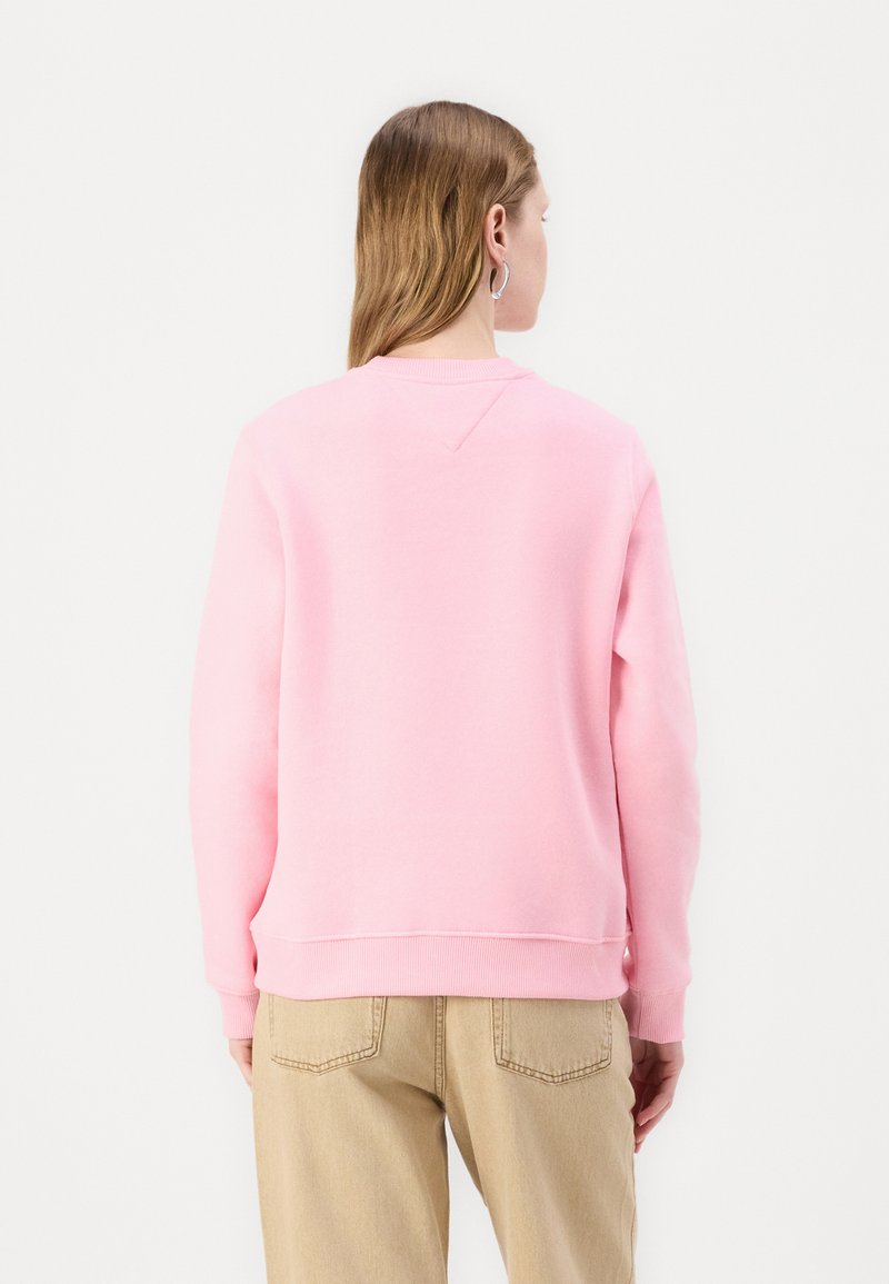 Felpa rosa con collo a giro, polsini e orlo a costine. Il retro presenta un dettaglio a yoke a forma di V. Abbinata a pantaloni beige chiaro.