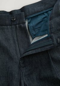 Denimové kalhoty v tmavě modré barvě, strukturovaná látka, přední zapínání na knoflík a modrá podšívka s skrytým zipovým kapsou.