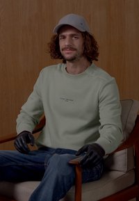 Mintgrønn hettegenser med ribbestrikkede mansjetter, med en liten logo på brystet. Mørke hansker og lys grå caps kompletterer blå jeans.