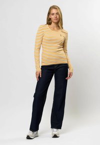 Cămașă cu dungi galbene și albe, cu mânecă lungă, decolteu rotund, design ajustat, din material de bumbac, asortată cu blugi largi bleu închis și adidași.