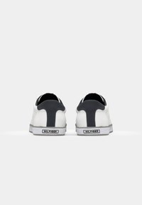 Witte canvas sneakers met een donkergrijze hielcounter, contrasterende stiksels, rubberen buitenzool en logo op de hiel. Minimalistisch ontwerp.
