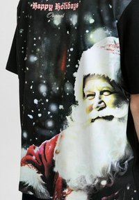 Sort kortærmet t-shirt med et stort grafisk motiv af julemanden med hvidt skæg, rød dragt og snefyldt baggrund, mærket "Glædelige helligdage".