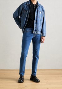 Jeansjacka med två bröstfickor, kombinerad med en mörk polo och ljusblå åtsittande jeans. Svarta läderskor fulländar outfiten.