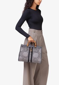 Borsa grigia con un motivo tessurizzato, hardware in tonalità oro e manici in stile bambù. Presenta una chiusura superiore e due strisce frontali.