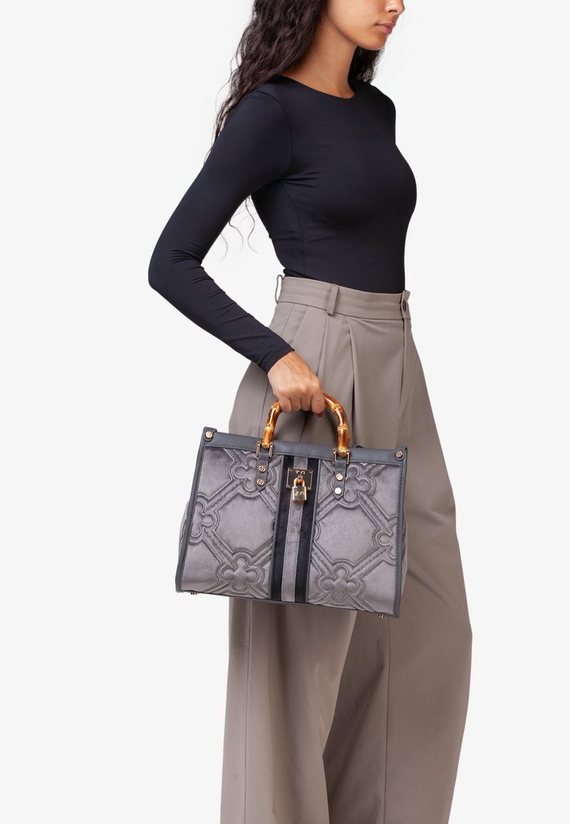 Borsa grigia con un motivo tessurizzato, hardware in tonalità oro e manici in stile bambù. Presenta una chiusura superiore e due strisce frontali.