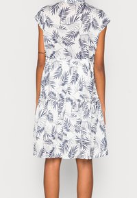 Witte jurk met een marineblauw bladmotief, korte mouwen, gelaagd ontwerp en zachte stof. Heeft een kraag en een ontspannen pasvorm.