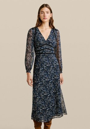 Vestido largo de estampado floral en color marino con mangas largas transparentes y escote en V. Presenta detalles fruncidos y una silueta tipo A. Textura suave.