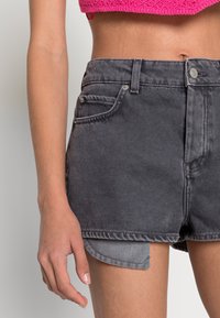 Shorts de denim gris con un acabado desgastado, cintura alta, bolsillos frontales y un dobladillo ligeramente desflecado. La costura visible acentúa el diseño.