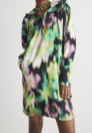 Person iført en flerfarvet grøn, sort, pink og hvid tie-dye hættetrøje med frontlynlås og en chunky guldkæde halskæde.
