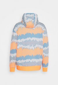 Hoodie med långa ärmar i orange, blå, vit och grå tie-dye-mönster med orangea ärmslut och midja, sedd bakifrån.