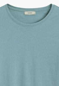 Jasnoniebieska koszulka z krótkim rękawem. Miękka, gładka faktura z okrągłym dekoltem. Metka czyta "ATLANTIC", rozmiar mały, umieszczona przy dekolcie.