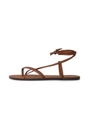 Sandale plate marron avec de fines lanières en cuir et un lien à nouer autour de la cheville, présentée sur un fond blanc.