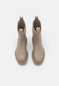 Botines beige de tobillo con upper de cuero liso, punta redonda y paneles laterales elásticos. Con tiradores y costuras alrededor de la suela.
