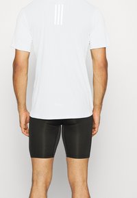 Camiseta atlética blanca con un acabado texturizado y tres franjas verticales en la parte trasera, combinada con pantalones cortos negros ajustados.