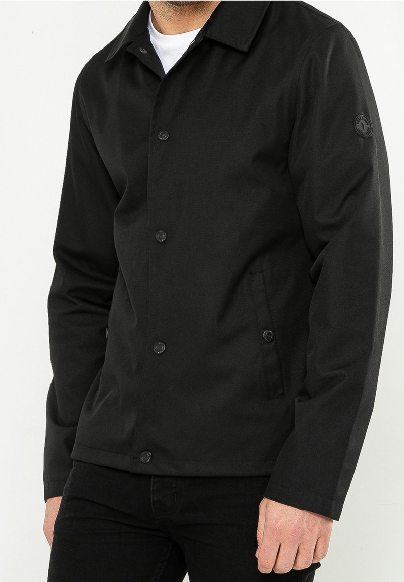 Czarna kurtka z teksturowanej tkaniny, zapinana na guziki, z wyprofilowanym kołnierzem i bocznymi kieszeniami, z naszywką logo na rękawie.