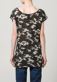 Volný tričko v camouflage vzoru, vyrobené z lehké tkaniny, s širokým výstřihem a krátkými rukávy. Barvy zahrnují tmavě zelenou a šedou.