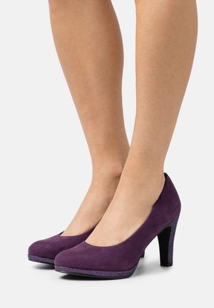 Escarpins en suédine violette avec un bout arrondi et une accent en paillettes violettes sur la semelle. Les talons présentent un design élégant et lisse.