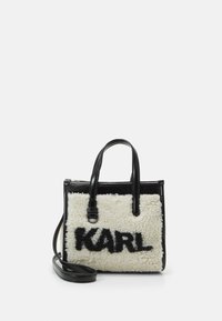 Sac fourre-tout noir et blanc avec une texture douce et pelucheuse portant le mot "KARL" en noir. Il dispose de deux poignées supérieures et d'une sangle d'épaule réglable.