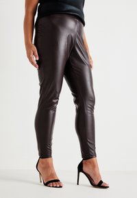 Brown faux leather leggings with a sleek, fitted design. Paired with black stiletto heels, showcasing a smooth texture and tailored shape.
