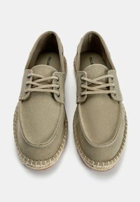 Beige vászoncipők lekerekített orral, fűzős stílusban, és szőtthajtogatták a talp mentén. Texturált felület és diszkrét varrási részletek.