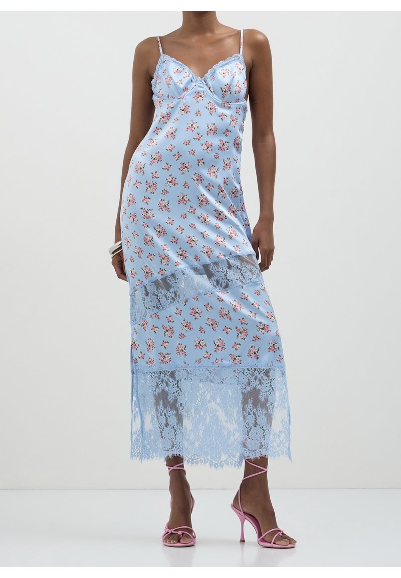 Robe nuisette sans manches bleu clair à imprimé floral avec inserts en dentelle portée avec des talons hauts roses à brides sur un mannequin debout.