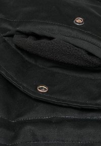 Gros plan sur une poche en tissu noir avec une fermeture à bouton-pression, révélant une doublure intérieure en polaire douce et texturée.