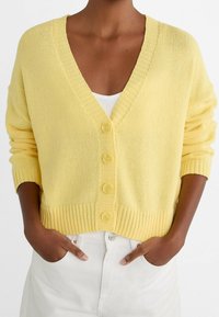 Yellow knitted cardigan with a V-neck, six buttons down the front, ribbed cuffs, and hem. Lightweight texture with a relaxed fit.