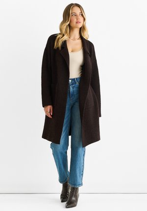 Brown wool coat with a loose fit and open front, paired with light blue high-waisted jeans. Model wears heeled boots, no visible patterns.