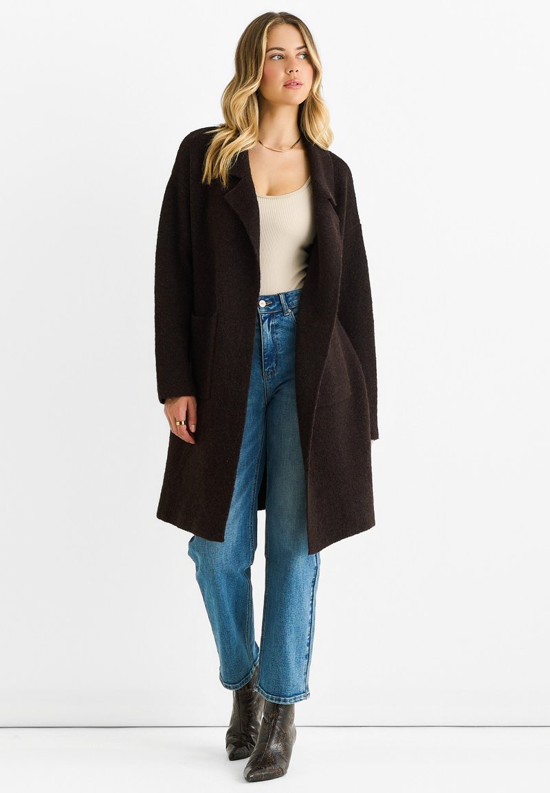 Brown wool coat with a loose fit and open front, paired with light blue high-waisted jeans. Model wears heeled boots, no visible patterns.