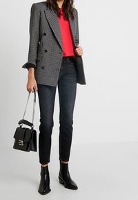 Czarny i biały w kratę podwójnie zapinany żakiet, czerwony top, czarne slim fit jeansy, czarne botki za kostkę oraz mała czarna torebka na łańcuszku.