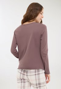 Top a maniche lunghe, color mauve, realizzato in un tessuto morbido, con scollatura rotonda e orlo a zig-zag, abbinato a pantaloni a quadri in colori tenui.