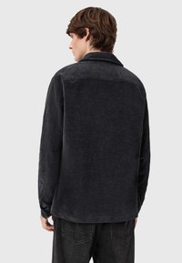 Tmavě šedá kordová bunda s límečkem, dlouhými rukávy a volným střihem. Má texturovanou látku a jednoduchý design bez ozdob.