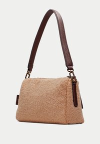 Sac en fausse fourrure couleur tan, de forme rectangulaire, avec une bandoulière en cuir texturé marron, des accessoires en or et un extérieur doux et duveteux.