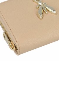 Beige strukturiertes Portemonnaie mit einem goldfarbenen Metallreißverschluss und einem dekorativen Anhänger. Es verfügt über eine glatte Oberfläche und eine kompakte rechteckige Form.