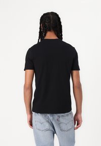 Chemise noire à manches courtes en coton doux, avec un col ras du cou et un ourlet droit, associée à un jean en denim délavé.