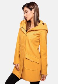 Chaqueta impermeable amarilla con capucha, con cierre frontal, bolsillos laterales y una textura suave. Incluye detalle del logo en el pecho.