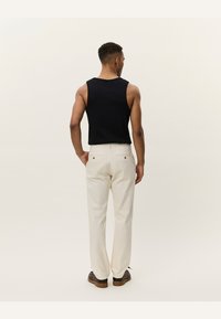 Top negru fără mâneci și pantaloni bej deschis, cu un design drept și două buzunare spate cu nasturi metalici.