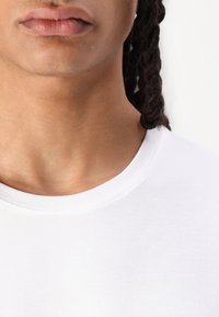 Bílý bavlněný tričko s kulatým výstřihem, hladká textura, přiléhavý design, se subtílními švy na límci a lemu.
