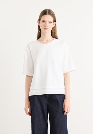 T-shirt blanc à manches courtes avec un col rond et un ourlet texturé, associé à un pantalon en denim large de couleur foncée.
