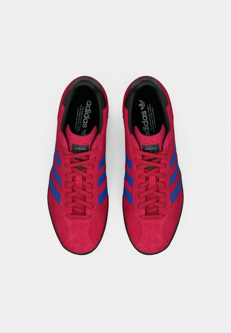 Baskets en daim rouge avec des rayures bleues, un bout rond, un devant à lacets et des accents noirs. Surface texturée avec des détails en matériaux contrastés.