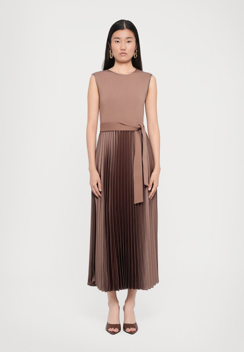 Brown, sleeveless midi dress with a pleated skirt and tied waist detail. Smooth, flowing fabric with subtle sheen. Worn with heeled shoes.
