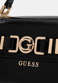 Borsa in pelle verniciata nera con chiusura logo dorata e dettagli in oro, dalla texture liscia e finitura lucida.