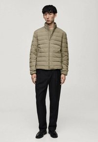Veste matelassée olive, design capitonné, fermeture éclair avant, col montant, associée à un pantalon noir et des chaussures noires. Look simple et fonctionnel.