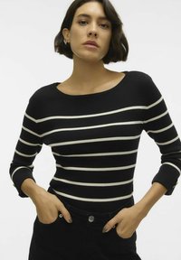 Must-valge triibuline ribidega sviiter, millel on lai kaelus ja kolmeveerandi pikkusega varrukad, ning millel on kuldsed nööpaktsentid varrukaotsas.