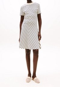 Randig A-linje klänning i krämfärg med marinblå v-format mönster, korta ärmar och rund halsringning, tillsammans med beiga vävda slip-on skor.