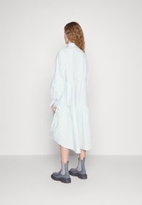 Ljusblå långärmad klänning i slätt tyg, med en lagerdesign och knäppning. Matchad med grå ankelstövlar.
