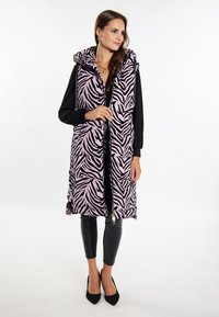 Gilet rembourré sans manches rose avec des rayures zèbres noires. Doté d'une capuche et d'une fermeture éclair à l'avant, associé à un pantalon en faux cuir noir et des talons.