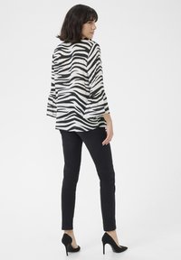 Blusa a righe zebra in bianco e nero con maniche a campana, abbinata a jeans skinny neri e tacchi alti neri, vista da dietro.