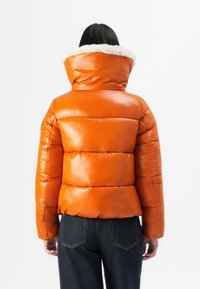 Orange puffer jacket with a shiny finish, featuring a white fur-lined collar and textured panels. Back view shows fitted silhouette.
